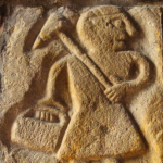 Image of a lead miner engraved in stone. He carries a pick and a box or bag.