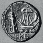 An ancient coin depicting a ship passing a lighthouse. Greek lettering can be seen at the bottom.