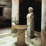 The entrance hall of a Roman bathhouse, with a marble floor, basin, bust of Apollo and two columns